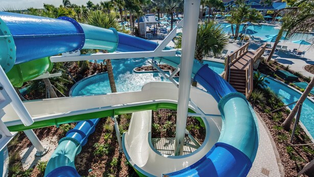 Een waterpark met glijbanen en zwembaden, omringd door palmbomen en ontspanningszones.
