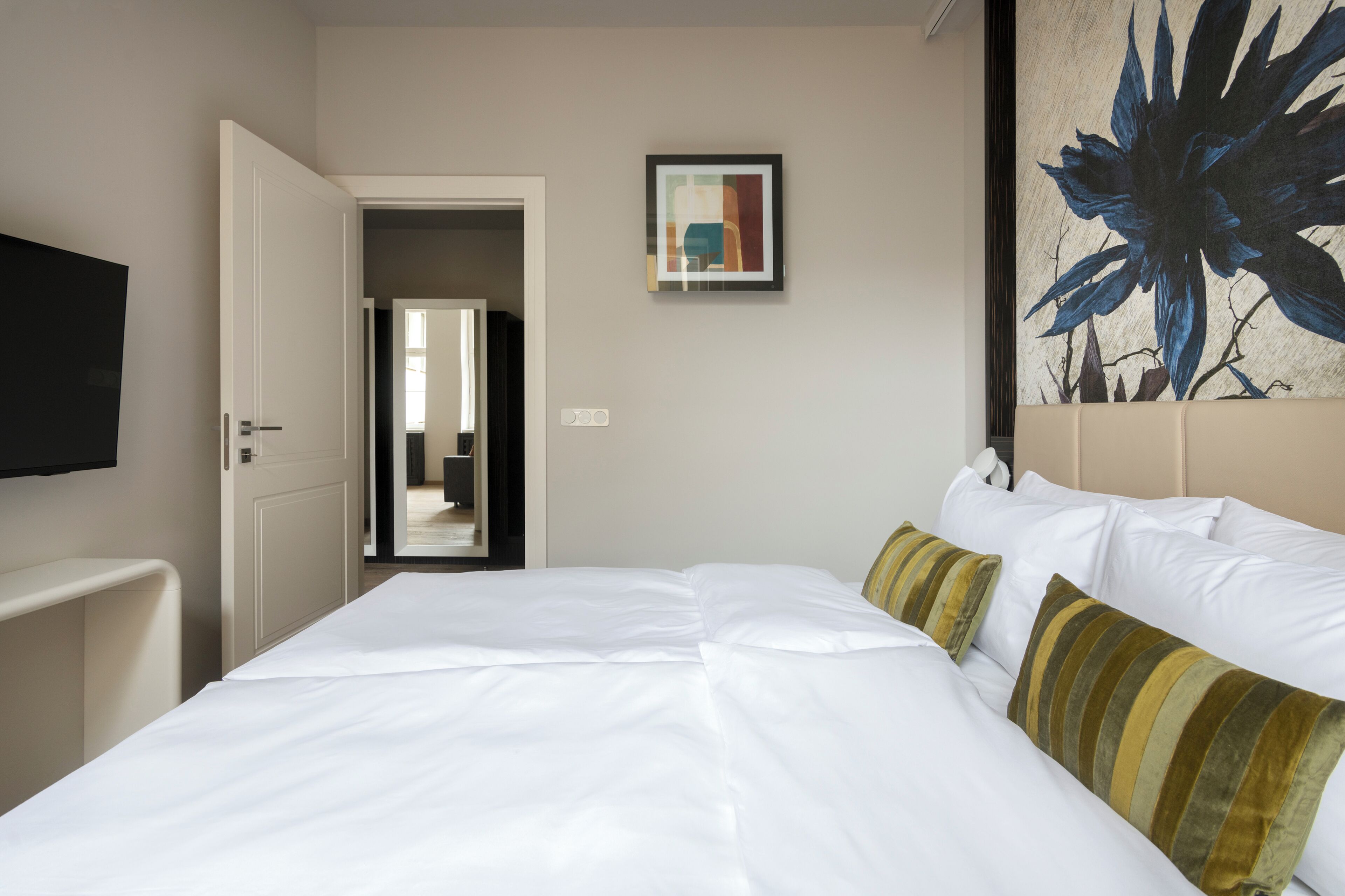 Une chambre d’hôtel avec un grand lit, un téléviseur à écran plat fixé au mur et une porte donnant sur une autre pièce.