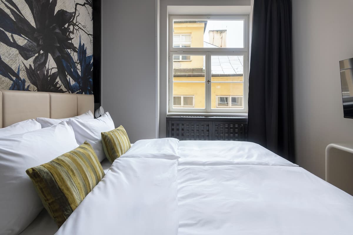 Une chambre d’hôtel avec un grand lit, une vue sur les immeubles par la fenêtre et un tableau accroché au mur.