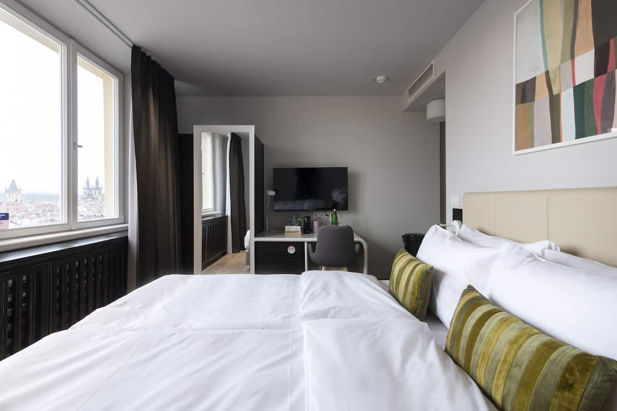 Une chambre d’hôtel avec un grand lit, un bureau, une chaise, une télévision et une fenêtre donnant sur la ville.