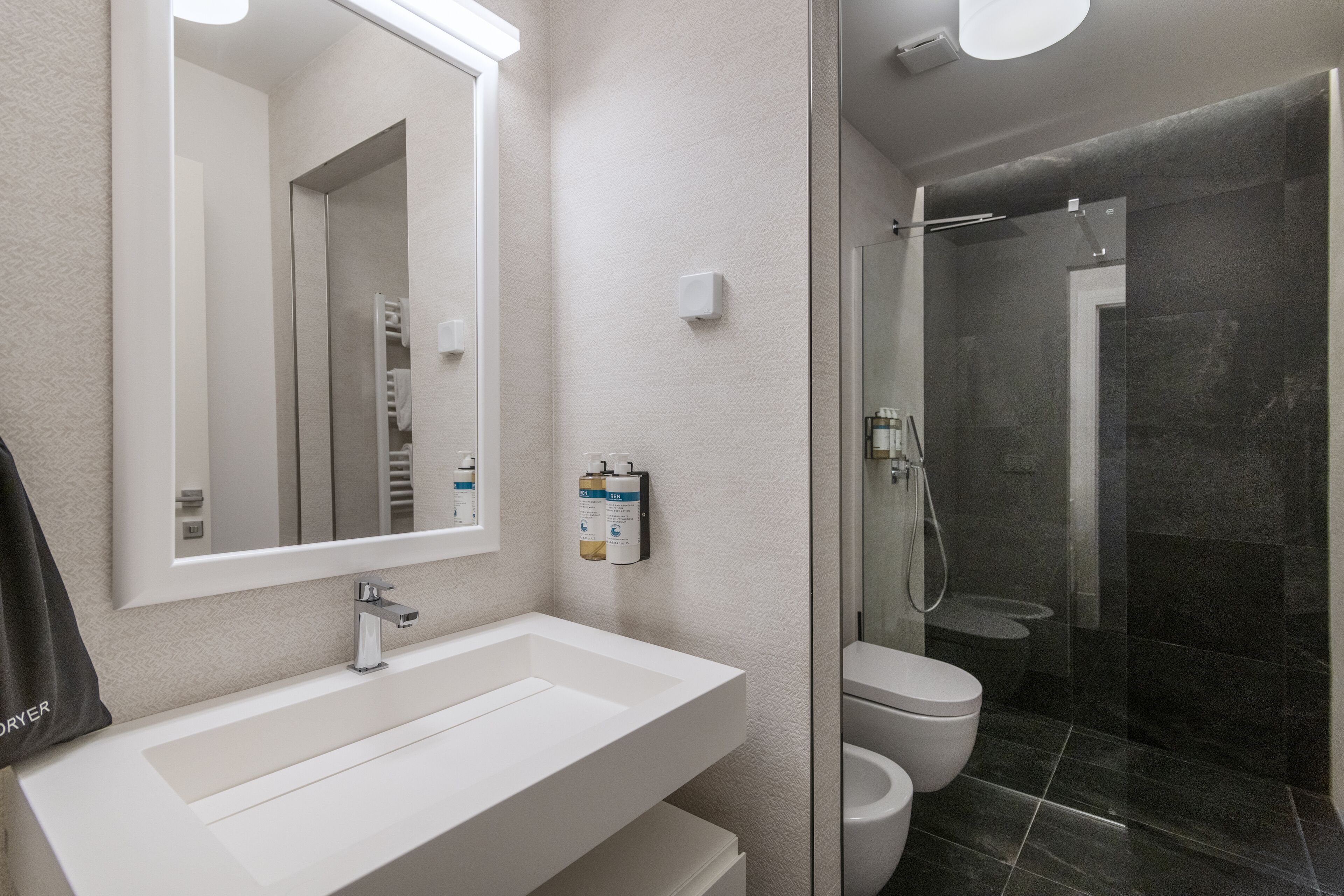 A modern bathroom with a large mirror, a white sink, a toilet, and a glass-enclosed shower area.