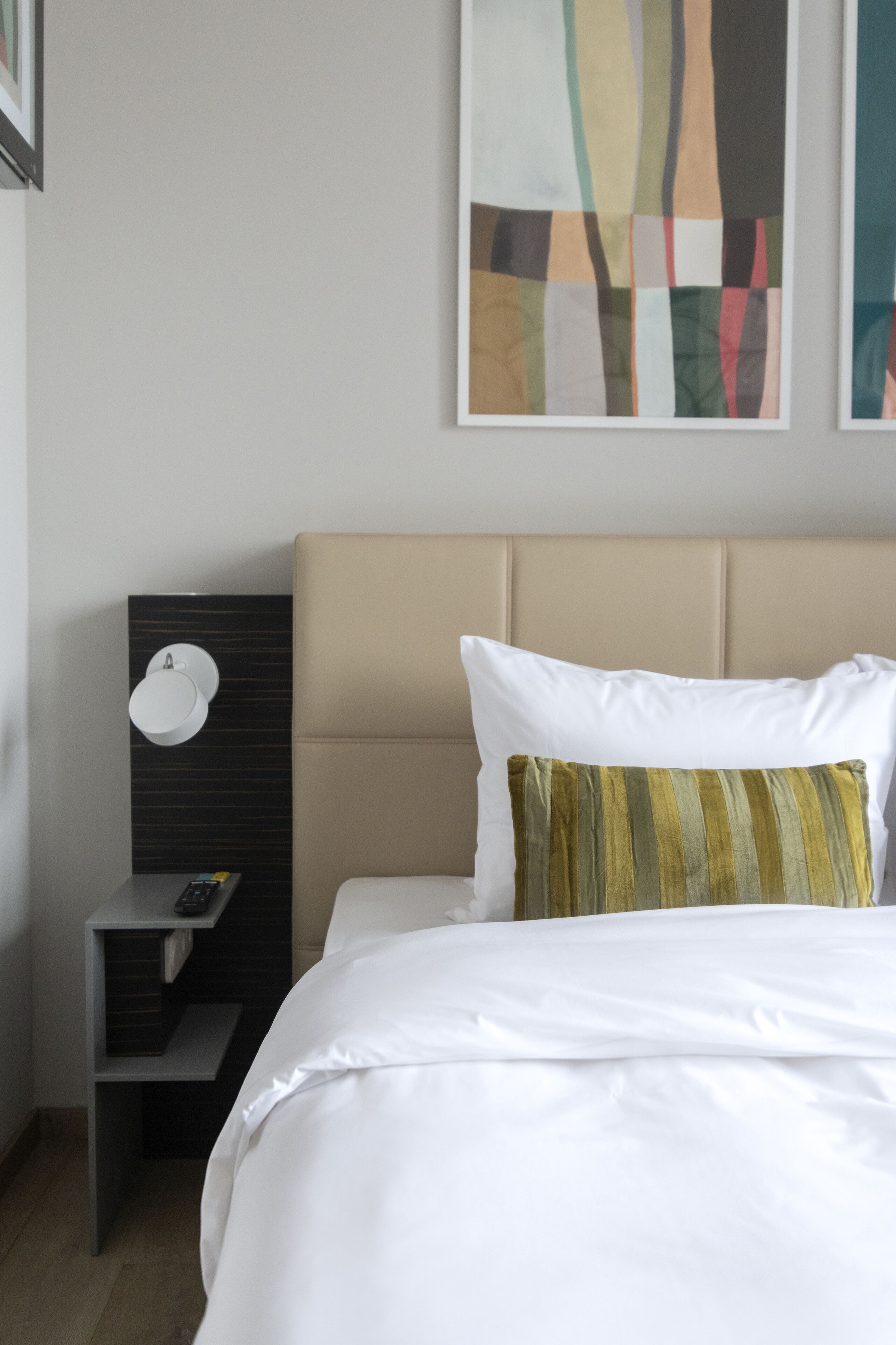 Une chambre d’hôtel avec un lit, une table de chevet avec une télécommande et une œuvre d’art abstraite au mur.