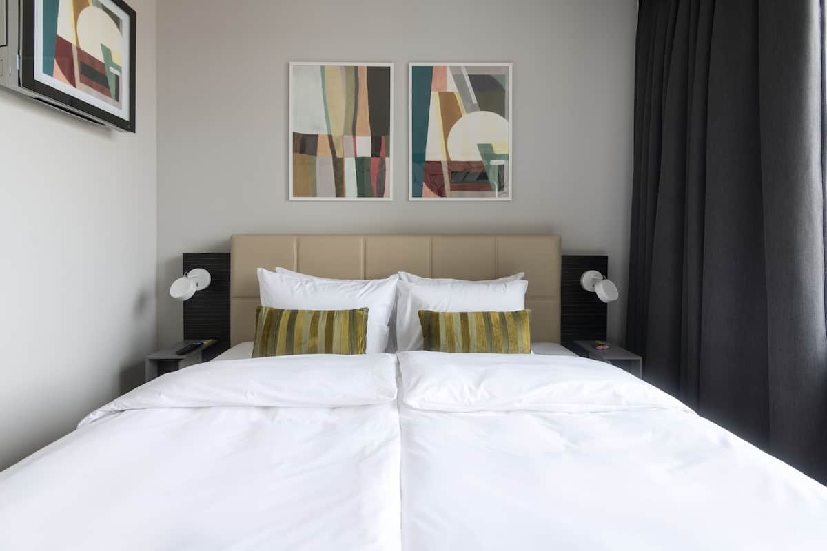 Une chambre d’hôtel avec un grand lit, deux tables de chevet et une œuvre d’art abstraite au mur.