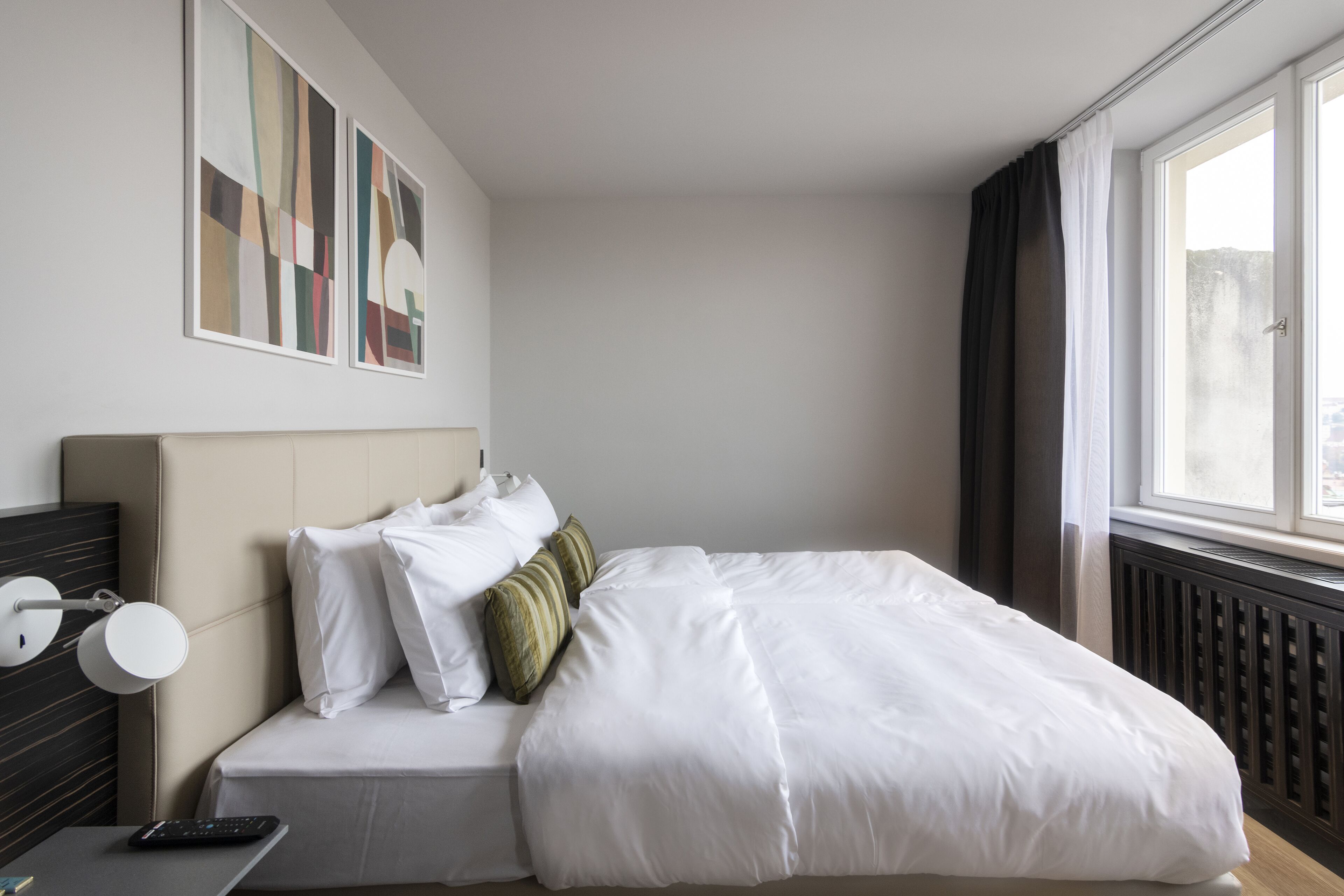 Habitació d'hotel amb llit, una taula de nit amb una làmpada, un comandament a distància i una obra d'art a la paret.