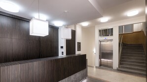 A modern reception area with a dark wood panel wall, a reception desk, and an elevator. - Numa Prague Poise (Prague)