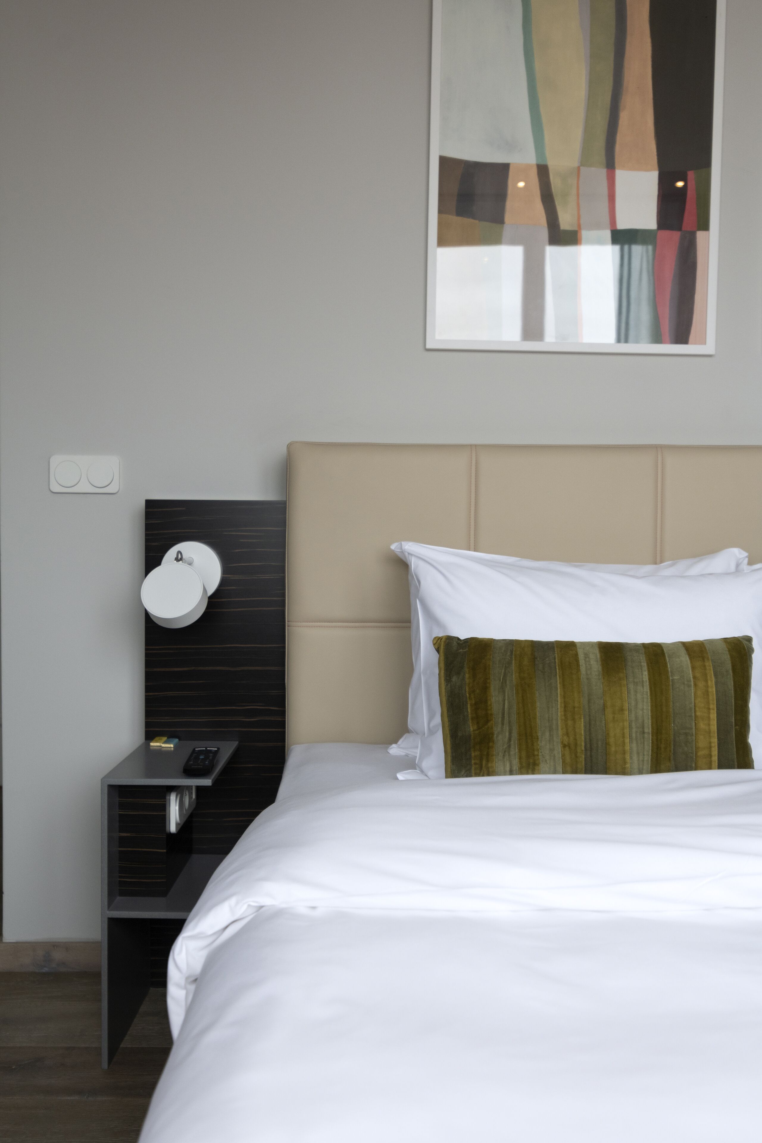 A hotel room with a bed, a nightstand, a lamp, and a wall art piece.