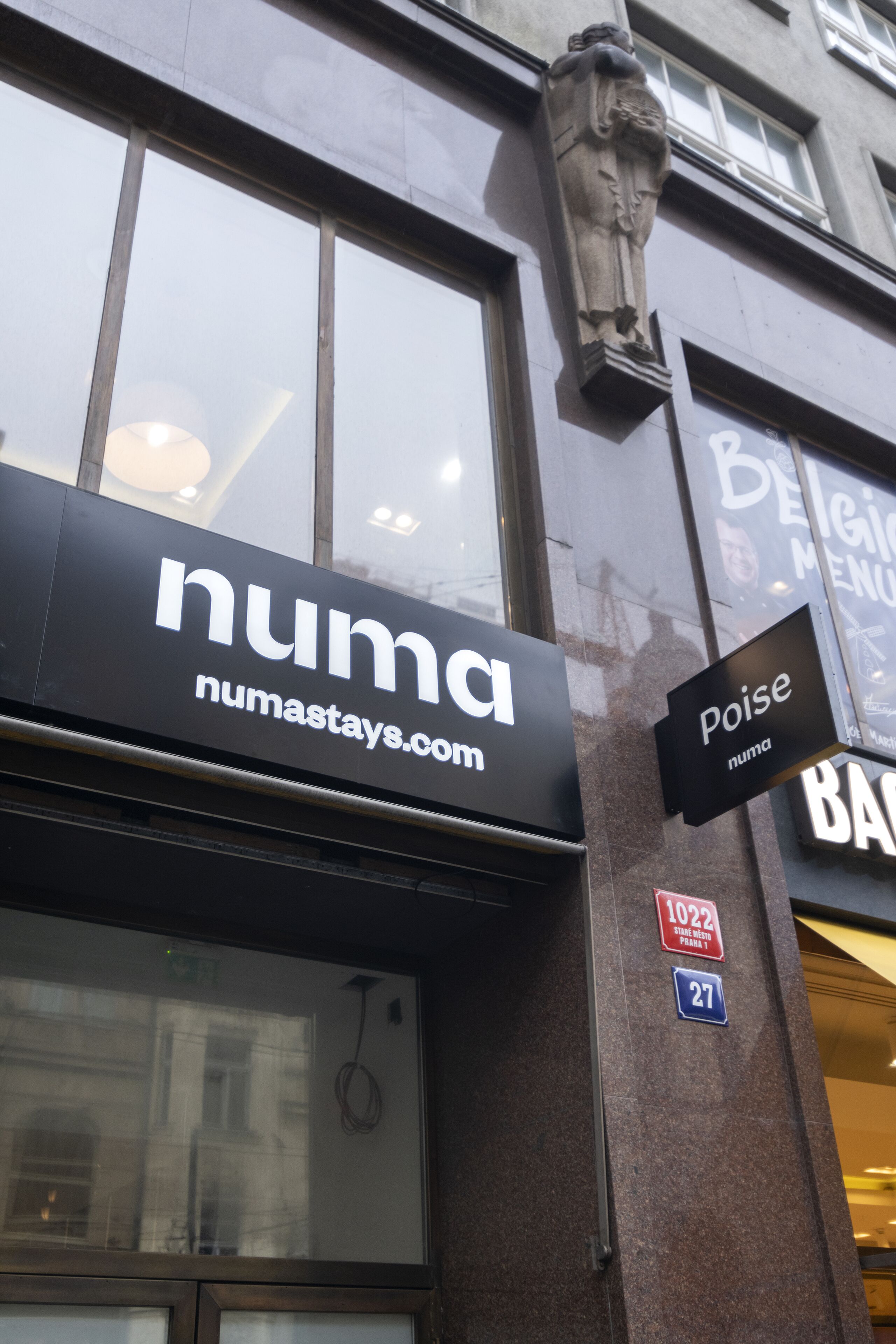 A building corner with a 'numastays.com' sign, a 'Poise' sign, and a '1022' address sign.