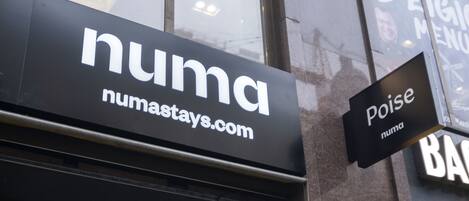 A building corner with a 'numastays.com' sign, a 'Poise' sign, and a '1022' address sign.