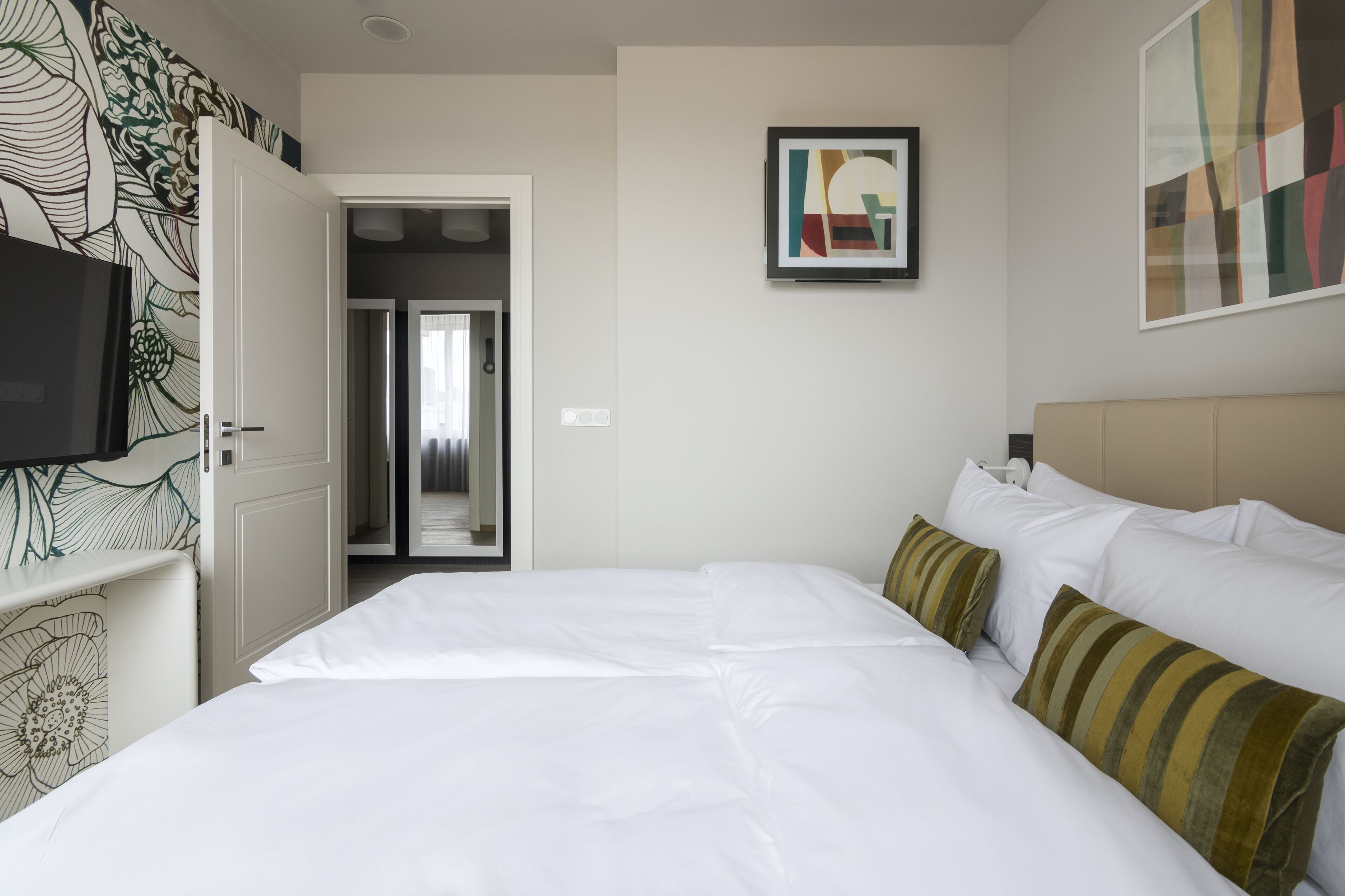 Une chambre d’hôtel avec un grand lit, une télévision et une porte donnant sur un couloir.