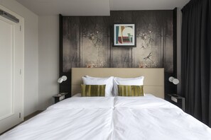 A hotel room with a large bed, a headboard with a framed artwork, a nightstand with a lamp, and a dark curtain. - Numa Prague Poise (Prague)