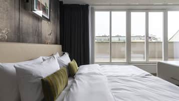 Een hotelkamer met een groot bed, uitzicht op de stad vanaf een balkon en een modern design.