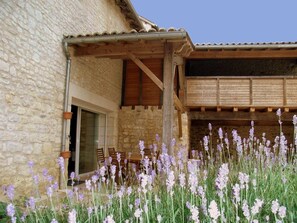 A stone building with a wooden porch and a garden with purple flowers. - Cottage with Heated Pool, Jacuzzi and Private Garden (Charras)