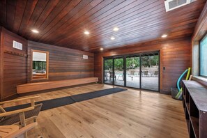 A room with wooden walls and ceiling, a bench, a chair, a large window, and a view of an outdoor patio area.