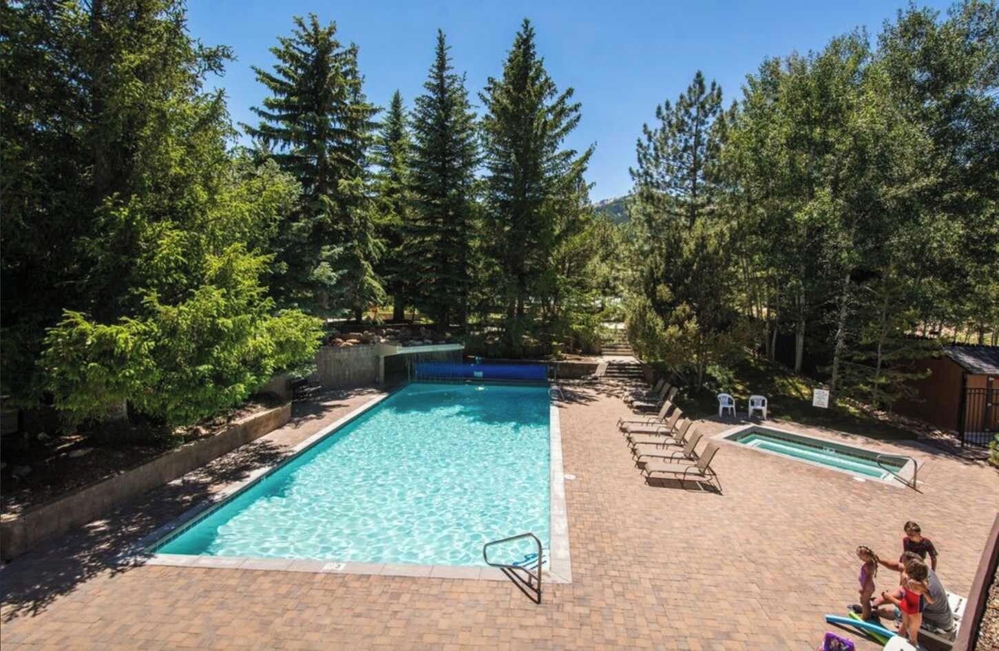 Ein rechteckiger Pool im Freien mit Sprungbrett, umgeben von Bäumen und einer Pflasterterrasse.