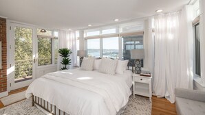 A spacious bedroom with a large bed, a nightstand, a lamp, and a view of the outdoors.