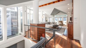 A spacious living area with a high ceiling, large windows, and a wooden staircase.