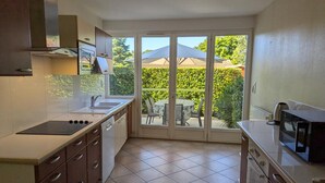 A compact kitchen with a built-in stove, a sink, and a microwave. It features a sliding glass door leading to a patio with outdoor seating. - Charming Cottage with Pool, Fireplace, and Garden in Vineyard Estate (Saint-Cybardeaux)