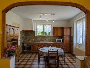 A kitchen with a checkered floor, wooden cabinets, a dining table set for four, and a window with a view of greenery.