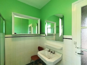 Une salle de bain avec des murs verts, des carreaux blancs, un lavabo blanc et deux miroirs.