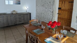 Een eetgedeelte met een houten tafel voor zes personen, een rustieke stenen muur en een houten deur.