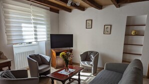 Een woonkamer met een bank, twee fauteuils, een salontafel, een televisie en een raam met zonwering.