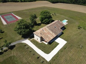 Vue aérienne d’une propriété comprenant un grand bâtiment, un court de tennis et une piscine.