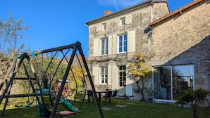 Ein Steinhaus mit einem großen Fenster und einer Schaukel im Garten.