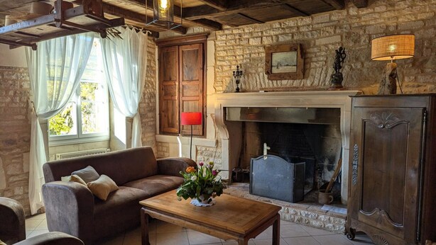 Ein rustikales Wohnzimmer mit Kamin aus Stein, Holzmöbeln und Blick auf Grünlandschaft.