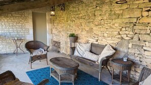 Ein Sitzbereich im Freien mit Steinwänden, Korbmöbeln und einem blau gemusterten Teppich.