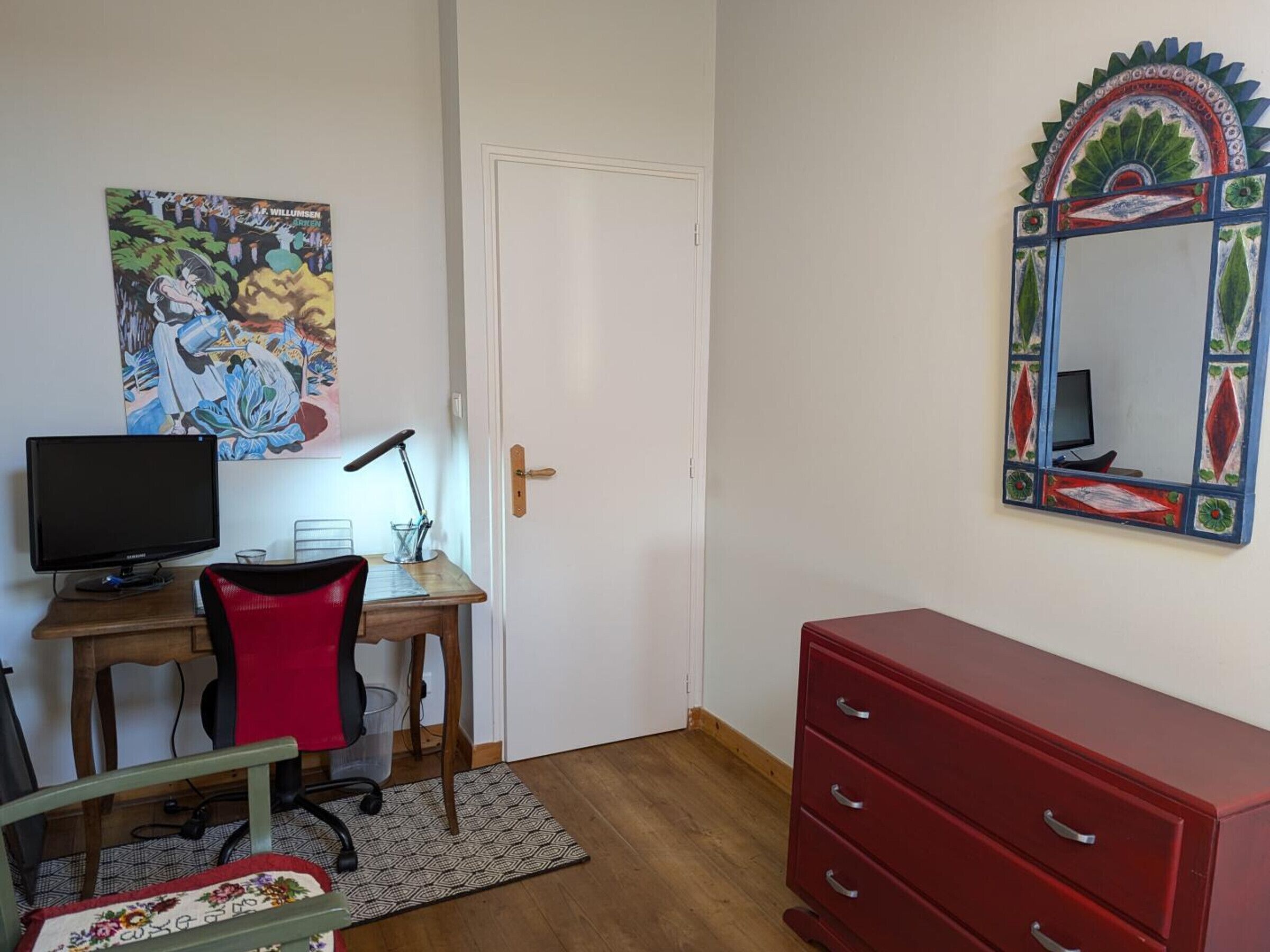 Una habitación con escritorio, silla, televisor y cómoda roja.
