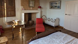 Ein Zimmer mit Holzboden, einem roten Sessel, einem Bett, einem Kamin und einem Gemälde an der Wand.