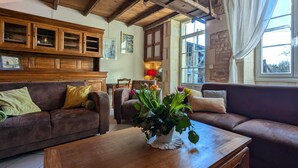 Ein gemütliches Wohnzimmer mit Holzmöbeln, einem Couchtisch mit floralem Mittelstück und Blick ins Freie durch große Fenster.