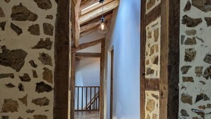 A hallway with exposed wooden beams, stone walls, and a staircase leading to an upper level. - Spacious house in Massignac with private garden (Massignac)