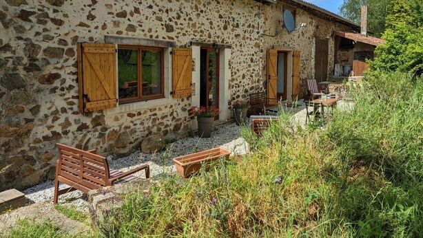 A rustic stone building with wooden shutters, a small outdoor seating area with benches, and a garden. - Spacious house in Massignac with private garden (Massignac)