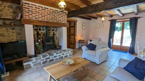 A cozy living room with a stone fireplace, wooden beams, a television, and comfortable seating. - Spacious house in Massignac with private garden (Massignac)