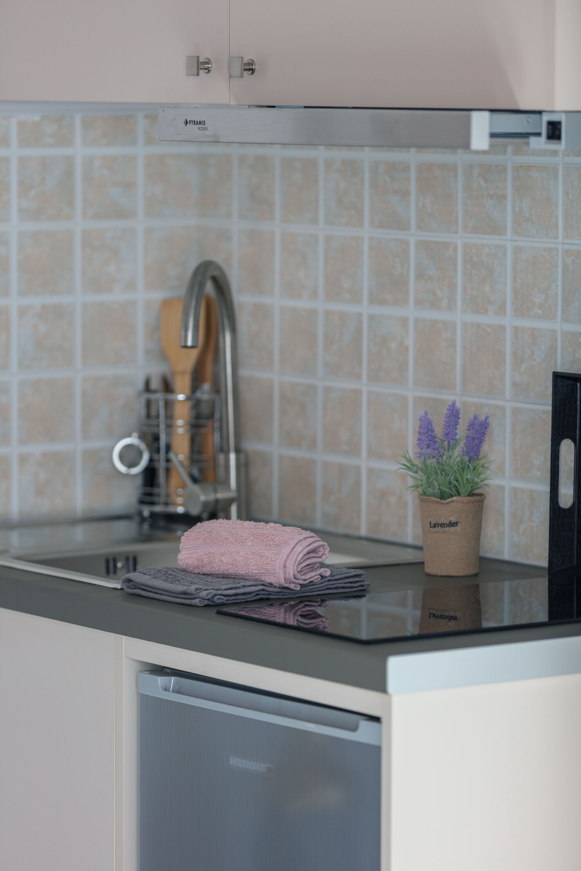 A kitchen with a stainless steel sink, a dish rack, a potted lavender plant, and a folded towel on the countertop.