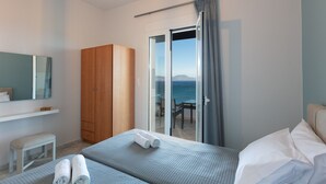 A bedroom with a bed, a wooden wardrobe, a small stool, and a sliding glass door leading to a balcony with a view of the sea. - Pietra Di Mare (Rethymno)