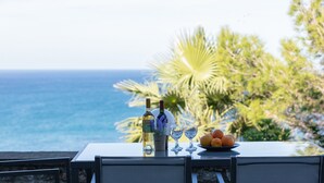 A table with a bottle, two glasses, and a plate of fruit by a scenic ocean view. - Pietra Di Mare (Rethymno)