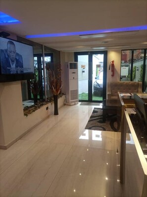 A modern lobby with a flat-screen TV, a reception desk, a sofa, and a fire extinguisher.