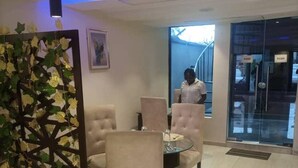 A modern hotel lobby with a glass entrance, a seating area with cushioned chairs, and a decorative plant wall. - Haven Suite (Lagos)