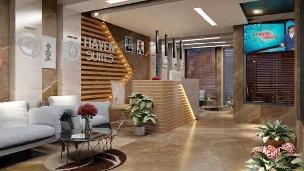 A modern hotel lobby with a reception desk, seating area, and a large screen displaying 'Imagine World'. - Haven Suite (Lagos)