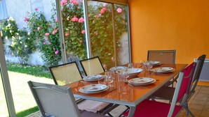 A dining area with a table set for four, chairs, and a view of a garden with pink roses through large windows. - Renovated Charente cottage with vineyard views, near Angoulême (Champagne-Vigny)