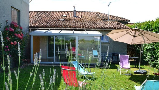 A house with a tiled roof, a glass-enclosed patio, and outdoor seating. - Renovated Charente cottage with vineyard views, near Angoulême (Champagne-Vigny)