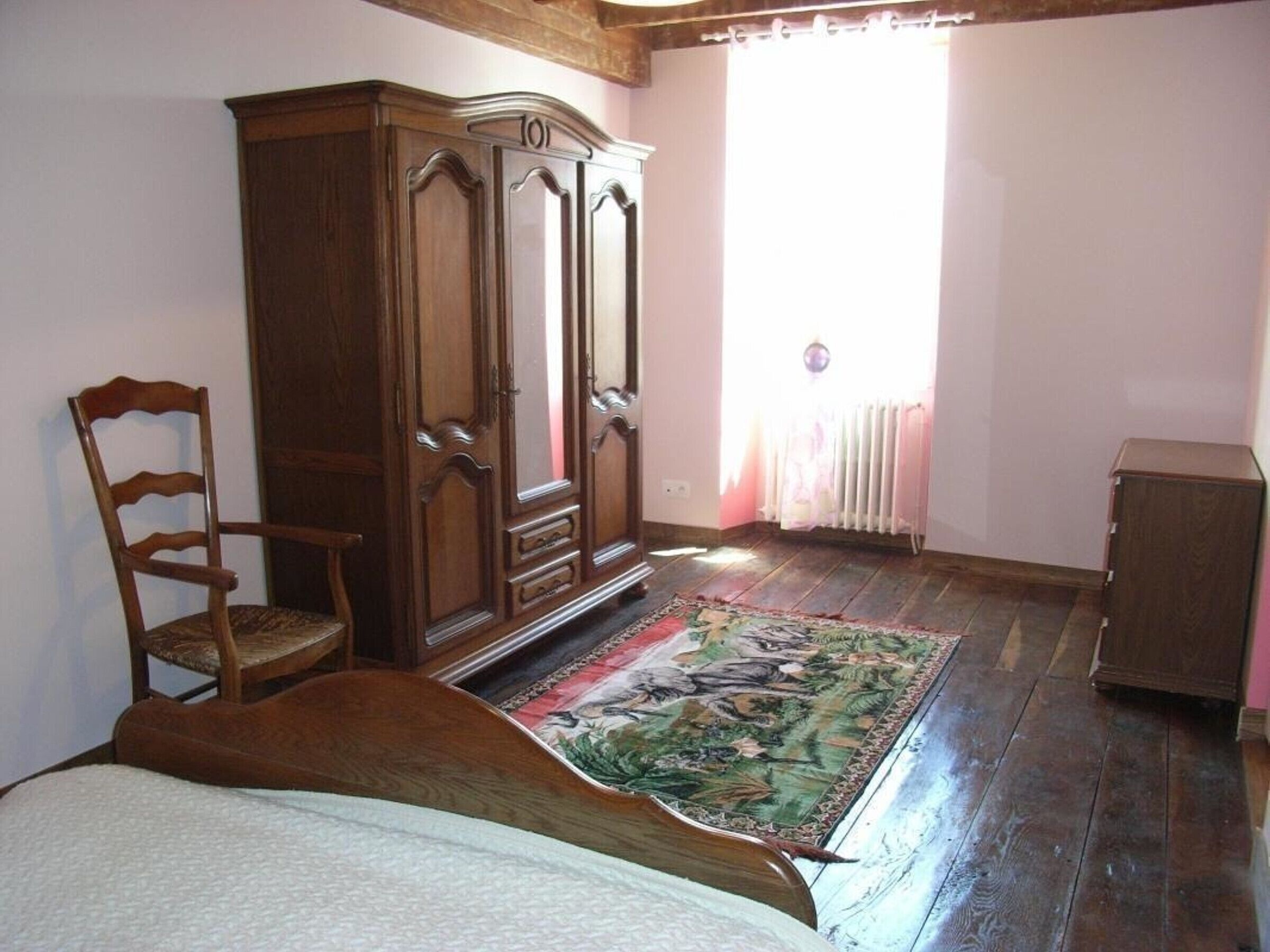 A bedroom with a wooden bed, a wooden wardrobe, a chair, and a radiator.