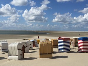 A beach with beach huts and a person walking on the sand. - Inselfriede Vacation Apartment: Quiet and Central in the Historic Center (Borkum)
