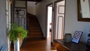 Un couloir avec un escalier en bois, une plante en pot, un banc en bois et un panneau encadré.