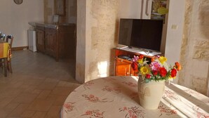 Un coin repas avec une table dressée pour quatre personnes, un buffet en bois, un téléviseur et un vase rempli de fleurs.