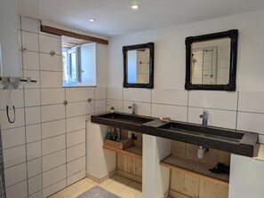 Une salle de bain aux murs recouverts de carreaux blancs, avec un meuble-lavabo en bois, un lavabo noir et deux miroirs dotés de cadres décoratifs.