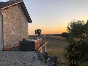 Un bâtiment en pierre doté d’un balcon donnant sur un champ, d’un jacuzzi et d’un palmier.