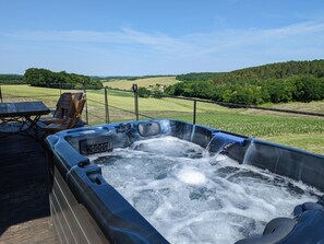 A hot tub with a wooden deck and chairs, surrounded by a fence and a view of green fields and hills. - Secluded house with private pool and spa, Charente (Montignac-le-Coq)